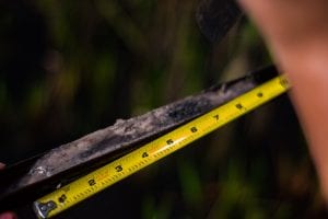 Close-up photo of a person measuring a dirty metal object with a yellow measuring tape.