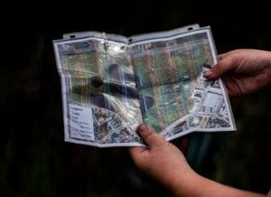 Hands holding a clear plastic-protected map in a natural outdoor setting.