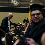 Graduates seated in a row at a ucf graduation ceremony, focusing on an elderly man shaking hands with a student.