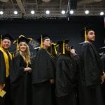 Group of diverse graduates in caps and gowns at a commencement ceremony, some smiling and looking forward.