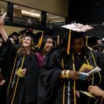 Graduates in caps and gowns celebrate during a commencement ceremony, with one throwing a cap in the air.