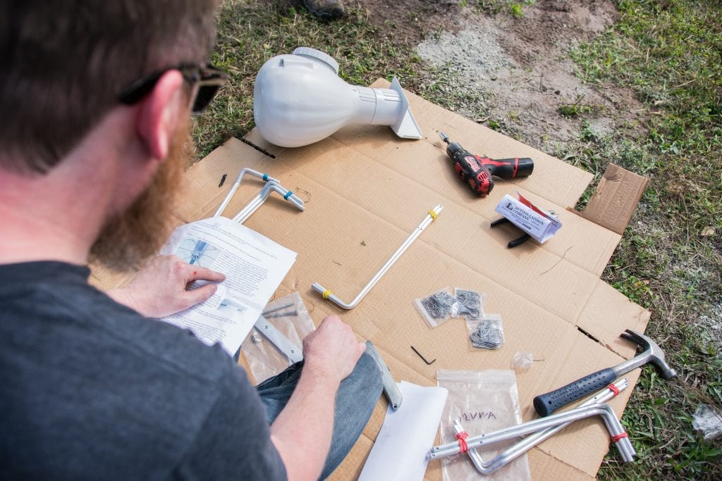 Man reading instructions while assembling furniture outdoors, with tools and disassembled parts on cardboard.