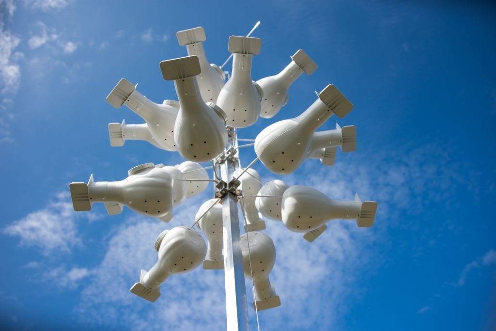 A cluster of white, inverted teapot sculptures forms an artistic installation against a bright blue sky with sparse clouds.