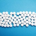 Rows of white round pills organized neatly on a blue background.