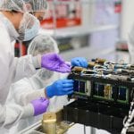 Two technicians in cleanroom suits assembling electronic components in a high-tech lab.