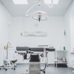 Interior of a modern, clean surgery room with an operating table, overhead surgical light, and various medical equipment.