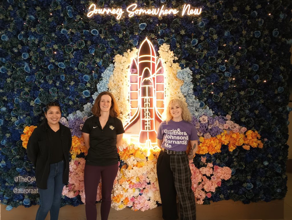 Three people who helped with the Conference for Undergraduate Women in Physics standing in front of rocket ship artwork 