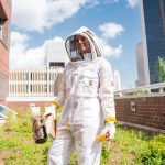 Tuesday piper stands in front of beehives in her bee suit
