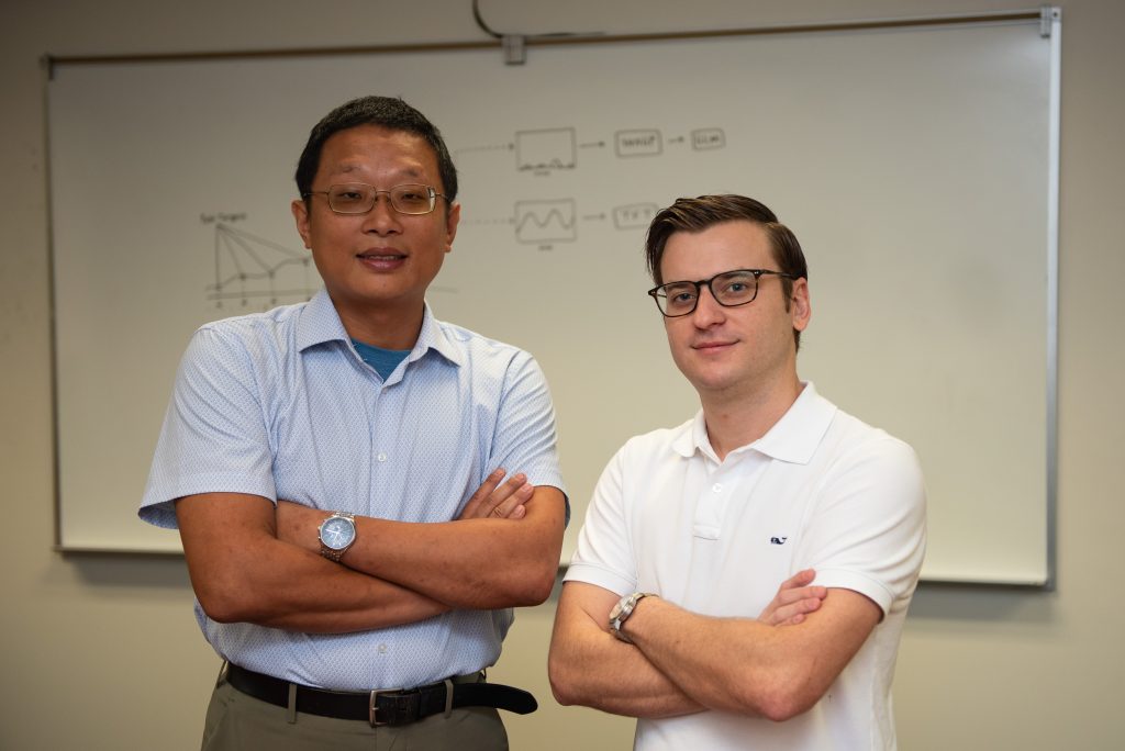 Associate Professor Hsin-Hsiung “Bill” Huang and student Hayden Hampton standing in front of whiteboard 