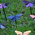 Six colorful manmade butterflies placed in grass, each butterfly with different patterns and hues.