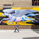 A person walks past a vibrant mural featuring a stylized winged horse.