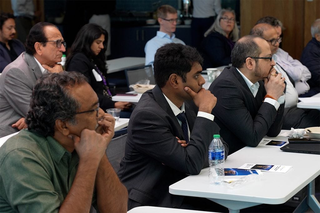 A group of people seated at tables, attentively listening to a presentation.