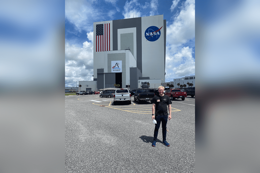 Person standing in a parking lot outside a large building with NASA and American flag logos.