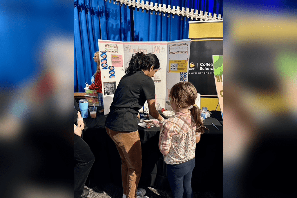 A woman explains science to a child at a booth with displays about DNA.