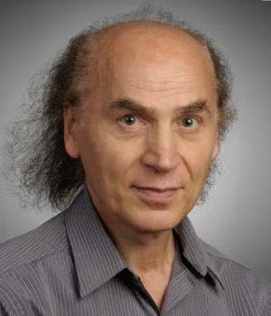 A middle-aged man with thinning hair and a striped shirt looks directly at the camera against a plain gray background.