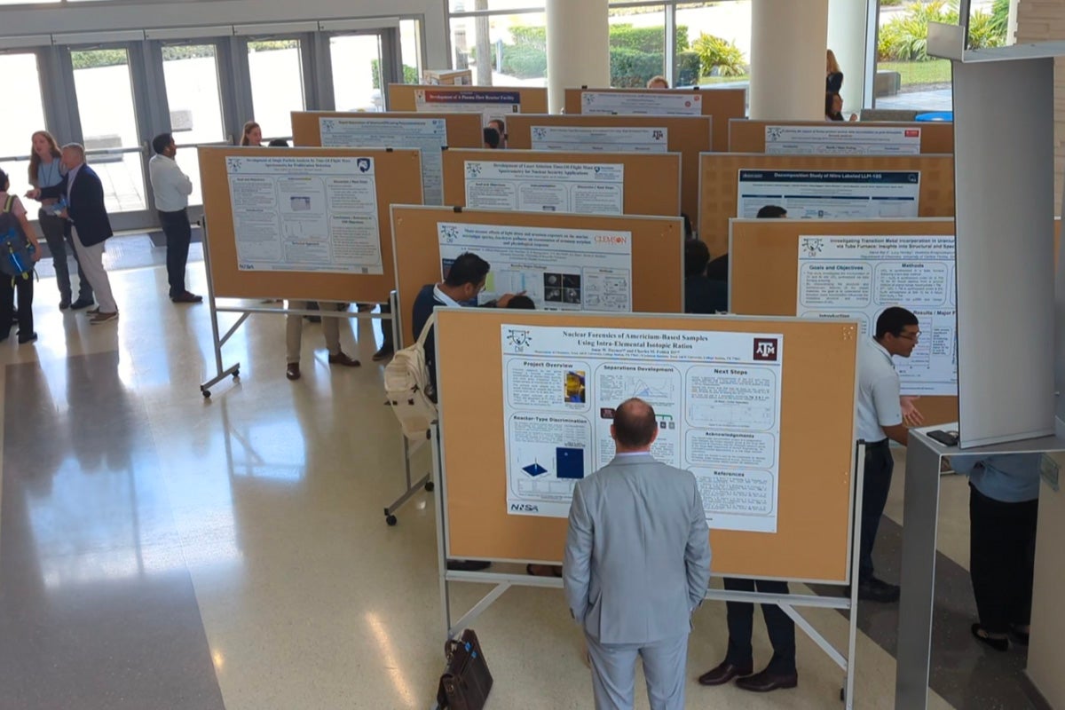 People view and discuss research posters displayed on boards at an indoor conference or academic event.