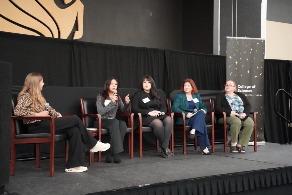 Five women sit on a stage panel, one speaking into a microphone, at a College of Sciences event at the University of Central Florida.