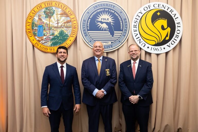 Three men in suits stand in front of official seals for the State of Florida, Florida Department of Law Enforcement, and University of Central Florida.
