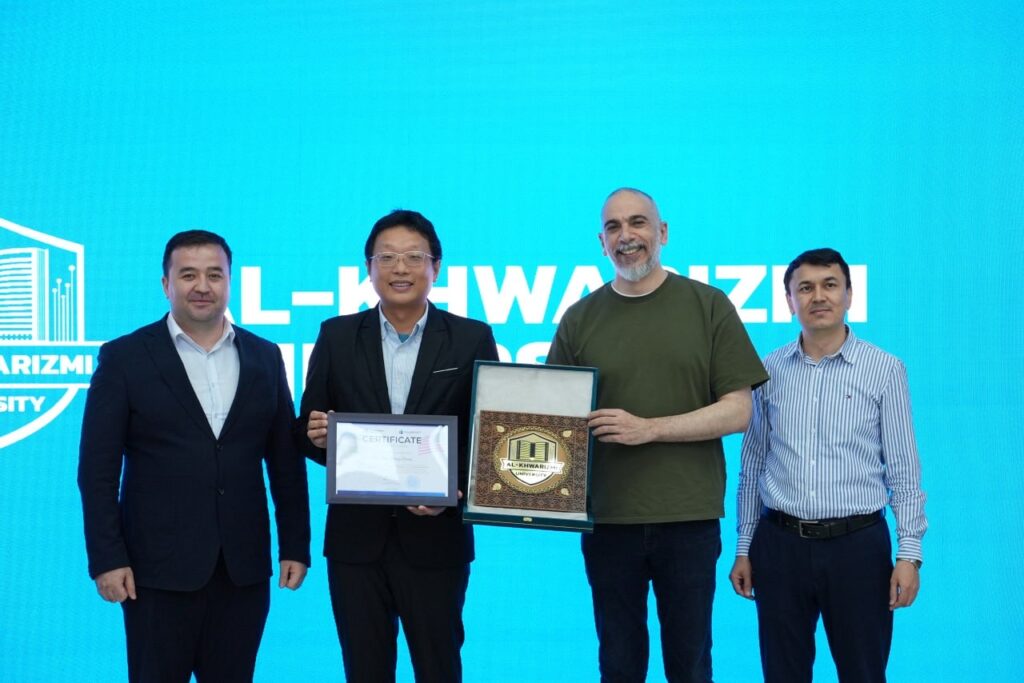 Four men stand in front of a blue background; two in the center hold a framed certificate and a decorative plaque, posing for a photo.