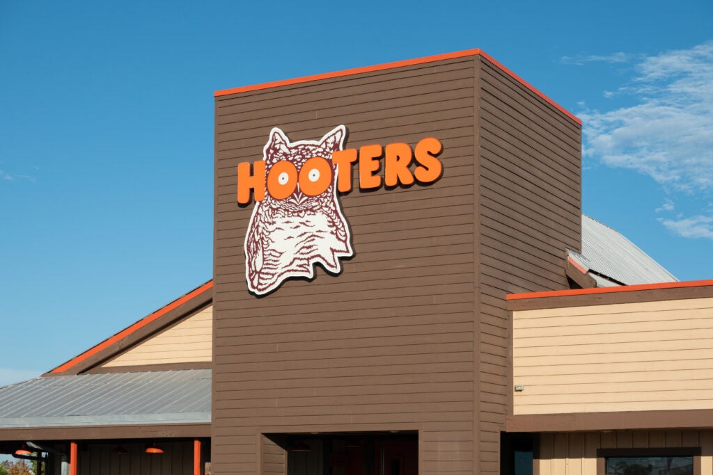 The exterior of a Hooters restaurant with a large orange and white logo featuring an owl on a brown section of the building.