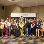 A group of University of Central Florida Department of Anthropology faculty and staff stand with the school’s Knight mascot in a conference room.
