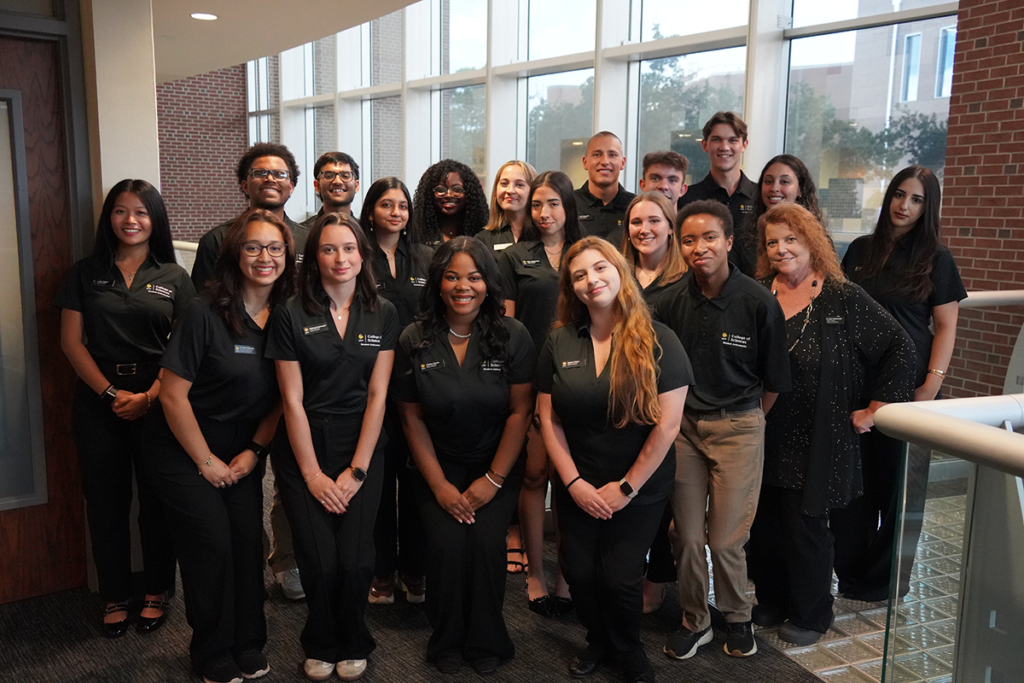 A group of students and staff in matching black polo shirts posing for a photo in an office building atrium.