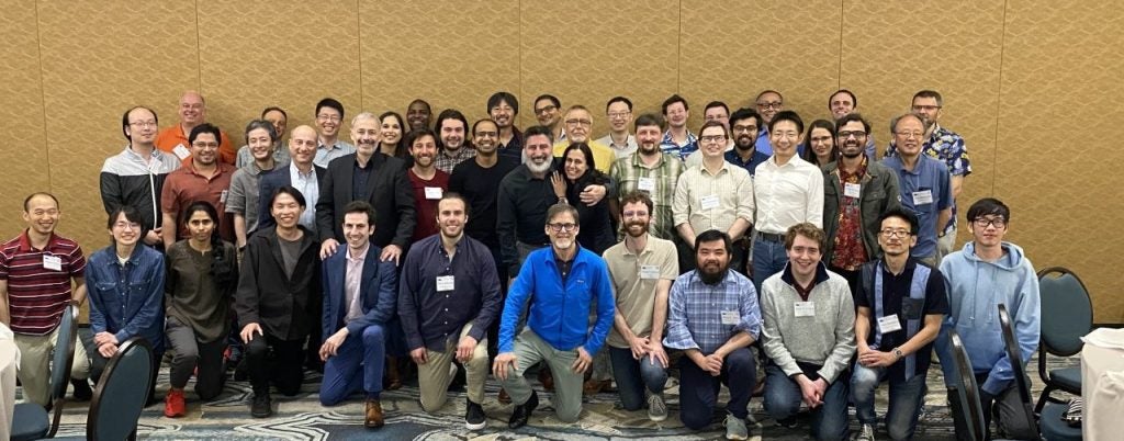 A diverse group of people posed together, many wearing name tags, in a conference room setting.