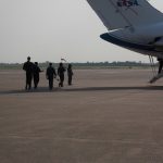 Five people in flight suits walk on an airport tarmac toward a NASA aircraft.