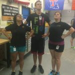 Three people stand in a workshop, posing with hands on their hips. An American flag and a Louisiana Tech University flag are hanging on the wall behind them.