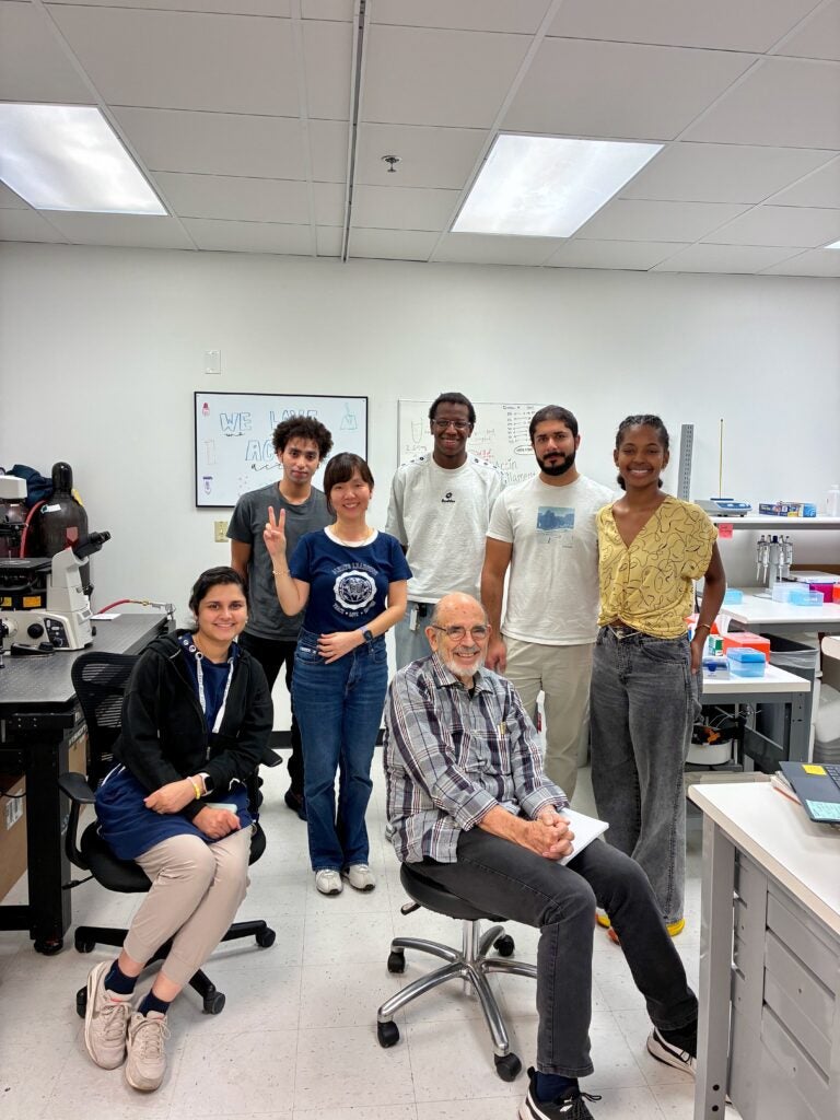 Seven people of various ages and backgrounds posing in a brightly lit laboratory.