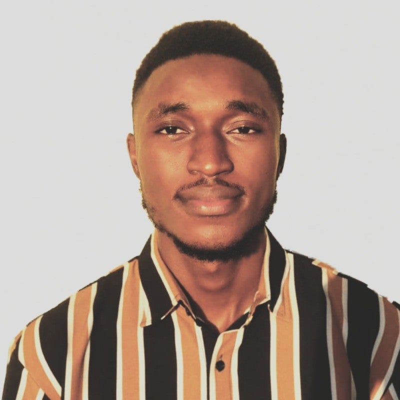 A man with short hair and a trimmed beard wears a black, white, and brown vertically striped shirt, posing against a plain light background.