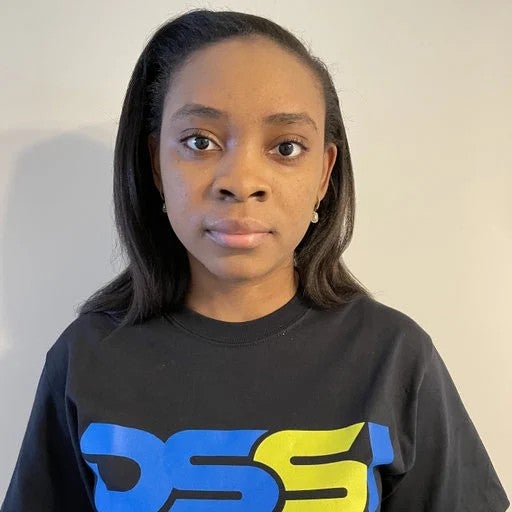 A woman with straight dark hair wearing a black DSS logo t-shirt stands against a plain light-colored background, looking directly at the camera.