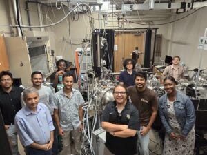 A group of eleven people stands in a laboratory surrounded by scientific equipment and machinery, posing and smiling for the camera.