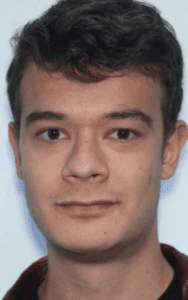 A young man with short brown hair and brown eyes looks directly at the camera against a plain light background.