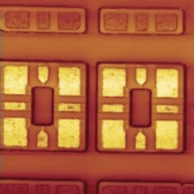 Close-up view of a computer microchip under a microscope, showing rectangular and square patterns with gold and copper hues.