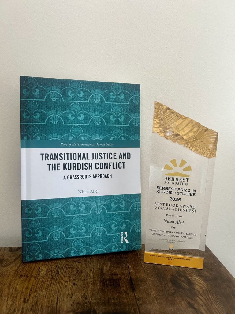 A book titled "Transitional Justice and the Kurdish Conflict" by Nisan Alici sits next to a Serbest Foundation award for Best Book in Kurdish Studies.