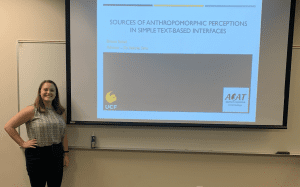 A person stands next to a presentation slide titled "Sources of Anthropomorphic Perceptions in Simple Text-Based Interfaces" with UCF and ACAT logos.