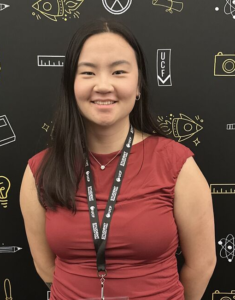 A young woman smiling in a red shirt and black pants, wearing a UCF Student name tag on a lanyard against a black backdrop with white and yellow school-themed icons.