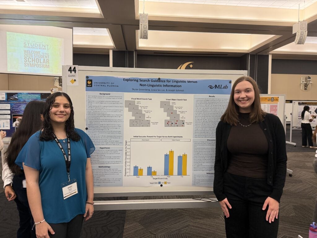 Two women stand in front of a research poster titled "Exploring Search Guidance for Linguistic Versus Non-Linguistic Information" at an academic conference.