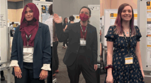 Three individuals stand in front of research posters at an academic event, each wearing a name badge and dressed in semi-formal or business attire.