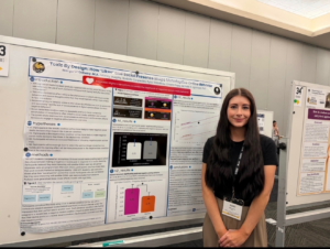 A woman stands and smiles in front of a scientific research poster titled "Toxic By Design: How 'Likes' and Social Presence Shape Interactivity on the Platform.