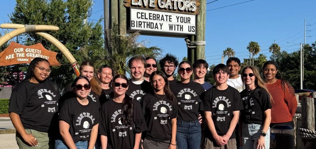 A group of people wearing matching black shirts stand together in front of a Congo River Golf sign on a sunny day.