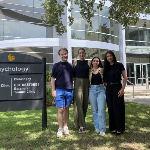 Four people stand in front of a building and sign for the UCF Psychology Clinic, Rosengren Trauma Clinic, and Philosophy department on a sunny day.