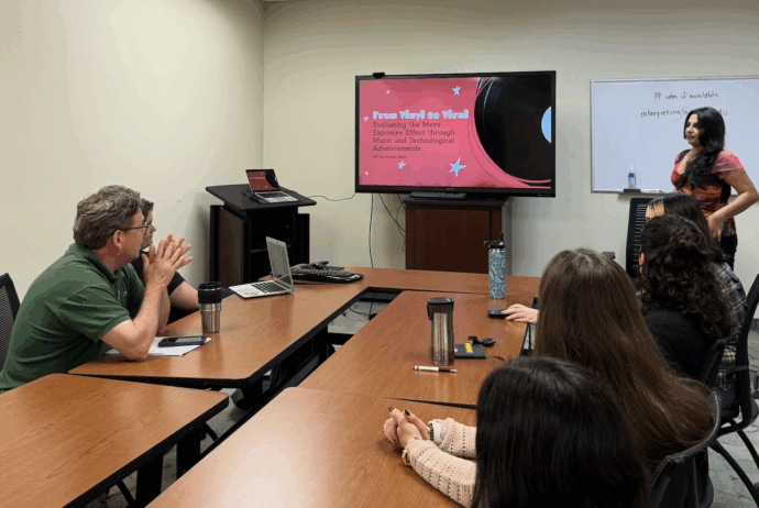 A woman presents a slideshow titled "From Vinyl to Viral" to a group of people seated around a conference table in a meeting room.