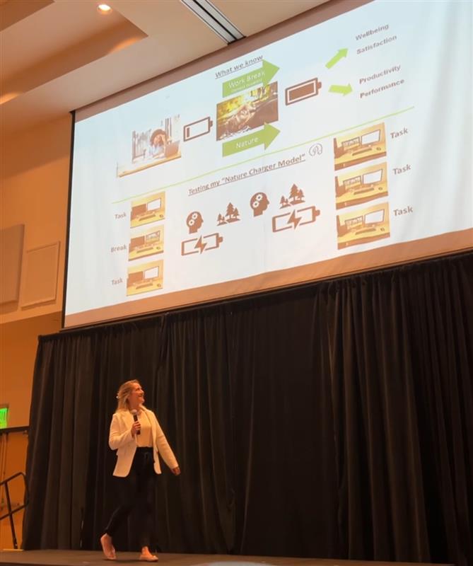 Person presenting a slide about the "Nature Charger Model" involving tasks and breaks for improved well-being, satisfaction, productivity, and performance.