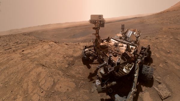 A Mars rover, the product of intricate undergraduate research, navigates the rocky Martian landscape under a hazy sky.