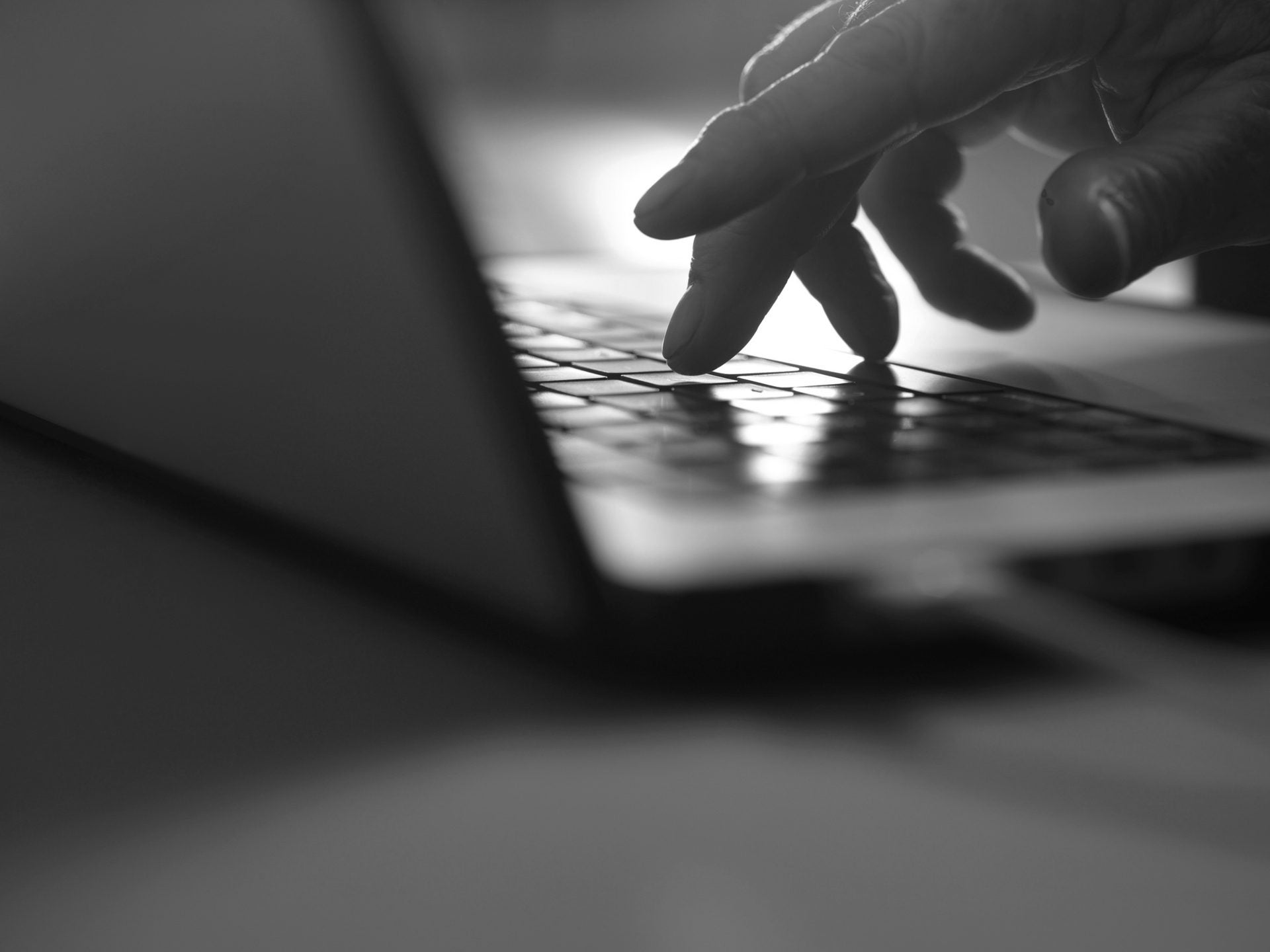 A close-up, black and white photo of a hand typing on a laptop keyboard.