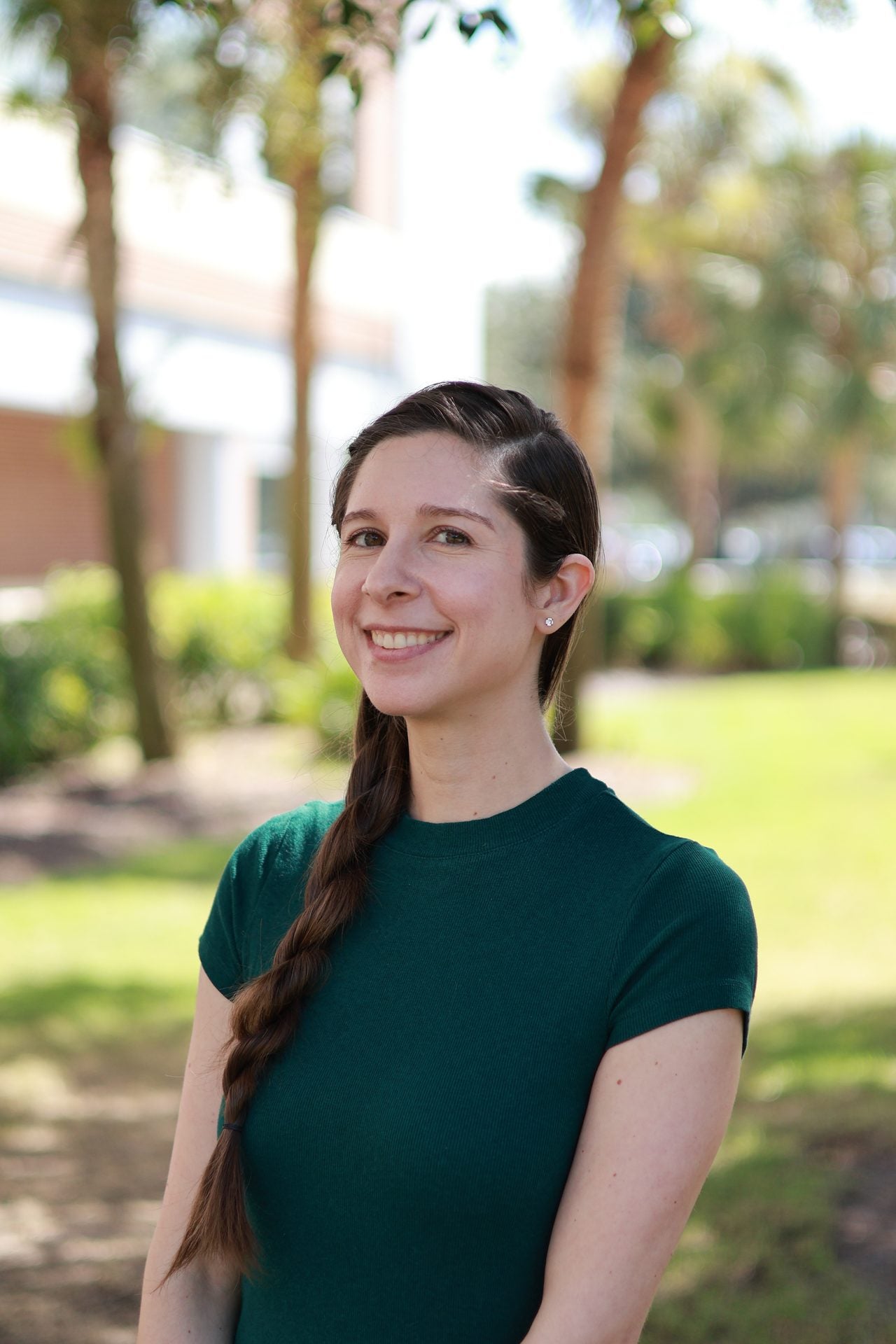 A smiling woman wearing a dark green t-shirt stands outside.