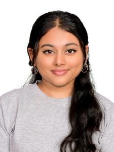 A person with long dark hair, wearing earrings and a light grey top, smiles at the camera against a plain white background.