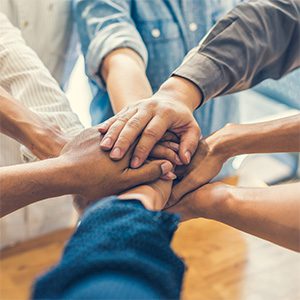 A group of people place their hands on top of each other in a gesture of unity and teamwork, with a blurred background.